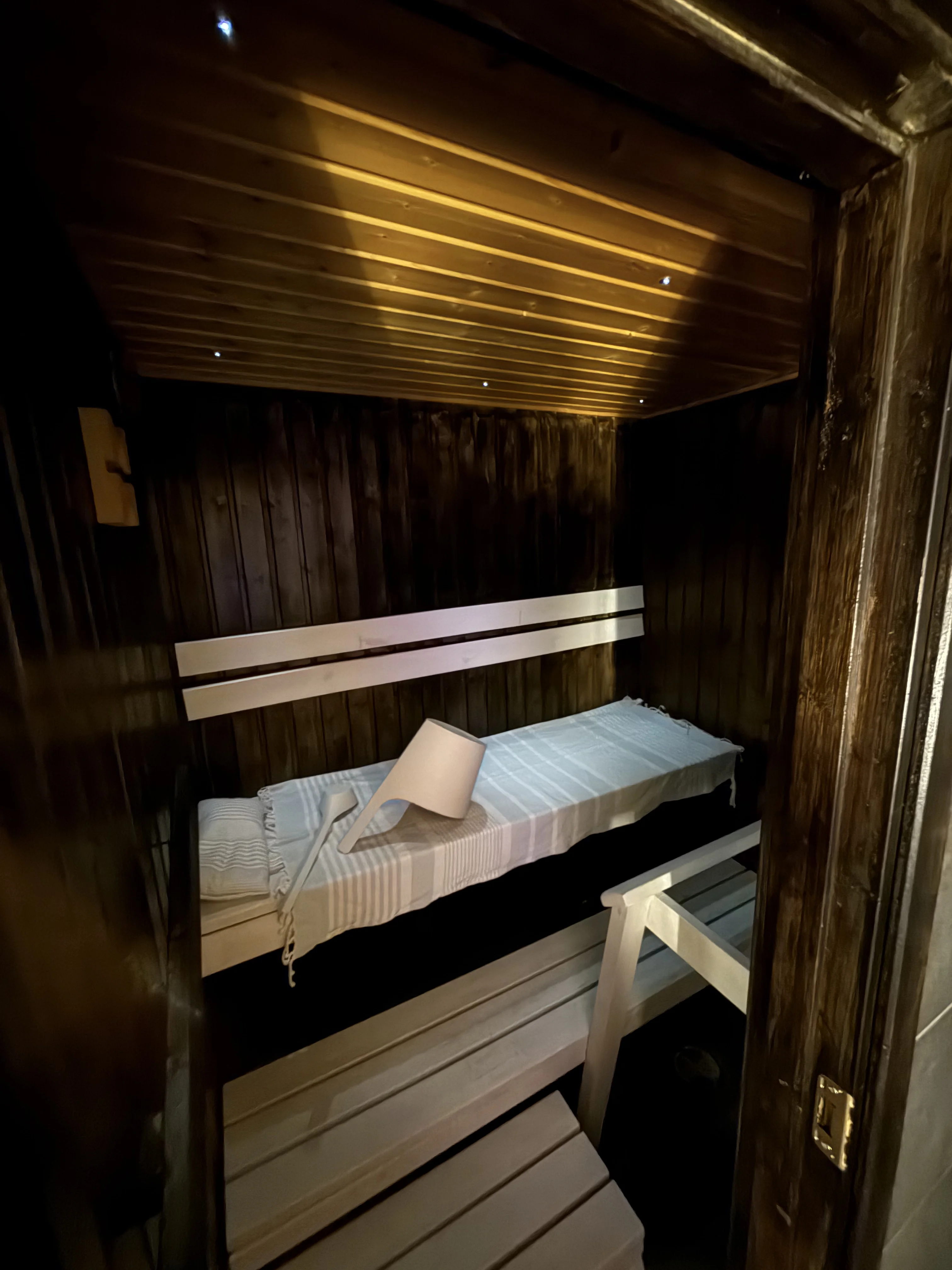 Inside the wood-panelled sauna, with a linen-covered bench and a wooden ladle